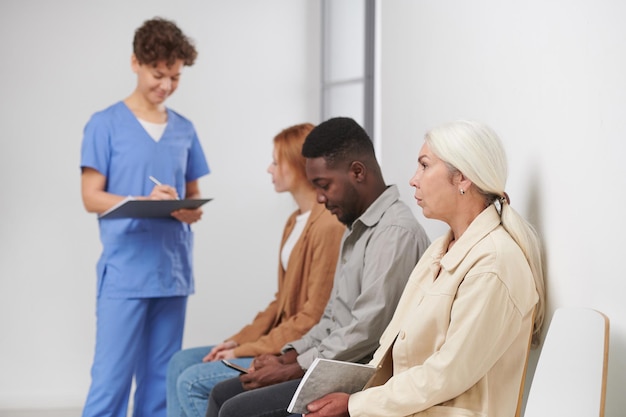 Groupe de trois personnes assises dans la file d'attente pour consultation dans l'hôpital moderne travailleur médical st