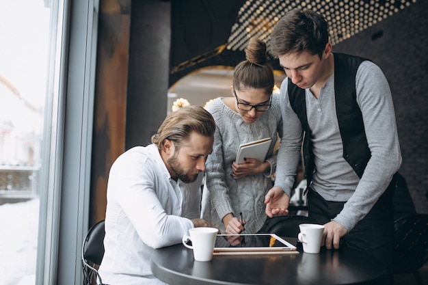 Groupe de trois personnes travaillant sur un projet sur une tablette dans un café