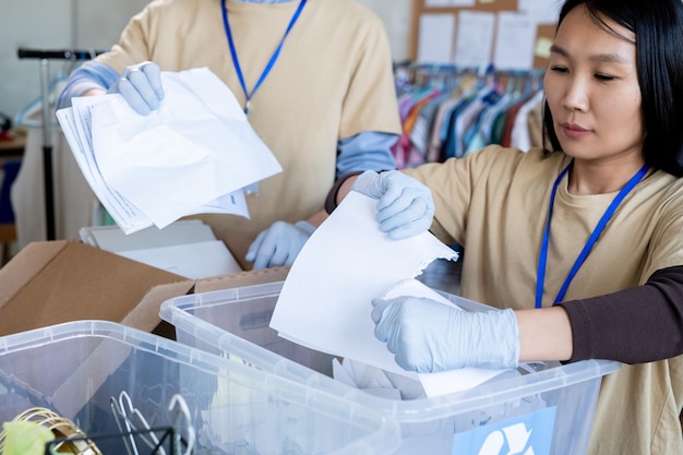 Groupe de volontaires dans des gants déchirant du papier sur des contenants en plastique