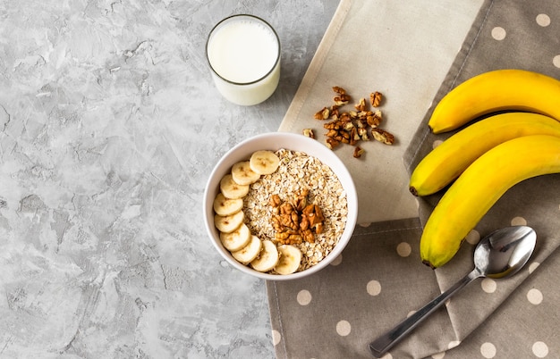 Gruau avec tranches de banane, noix et verre de lait sur table de ciment gris pour le petit déjeuner sur des serviettes en lin