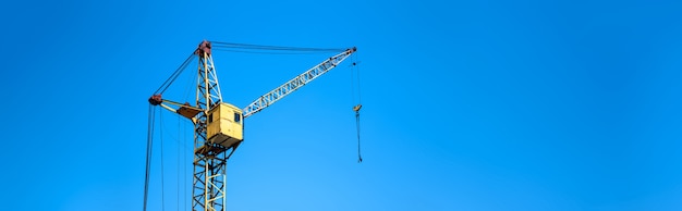 Grue d'ascenseur de construction jaune close-up contre le ciel bleu, maquette panoramique avec espace pour le texte