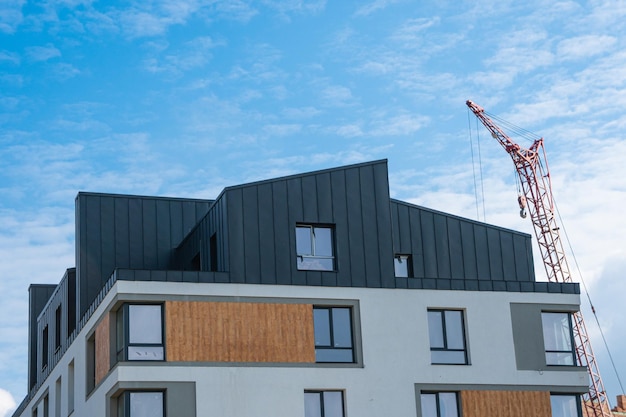 Grue et bâtiment. Une belle maison avec un toit noir sur fond de ciel bleu