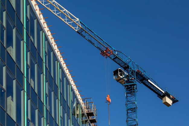 Grue bleue sur un chantier de construction contre un ciel bleu Construction d'une propriété commerciale Grande surface vitrée de façade