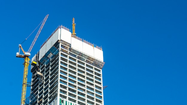 Grue et chantier de construction de bâtiment contre le ciel bleu avec panneau blanc blanc