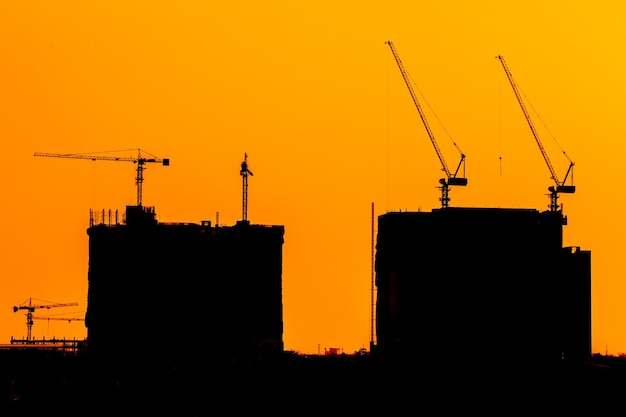 Grues de construction abstraites et silhouettes de construction au-dessus du soleil au lever du soleil