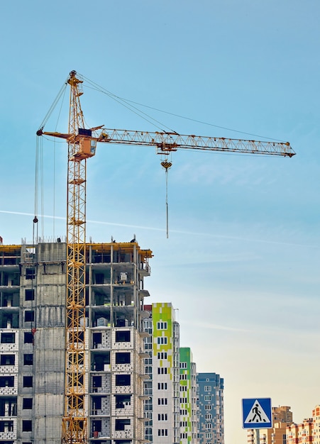 Grues de construction et immeuble d'habitation inachevé contre le ciel bleu. Image verticale.