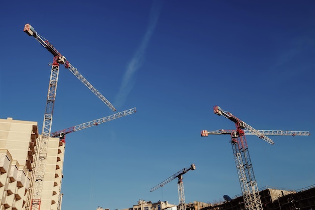 Les grues de construction travaillent sur le site de création sur fond de ciel bleu. Vue de dessous de la grue industrielle. Concept de construction d'immeubles à appartements et de rénovation de logements. Espace de copie