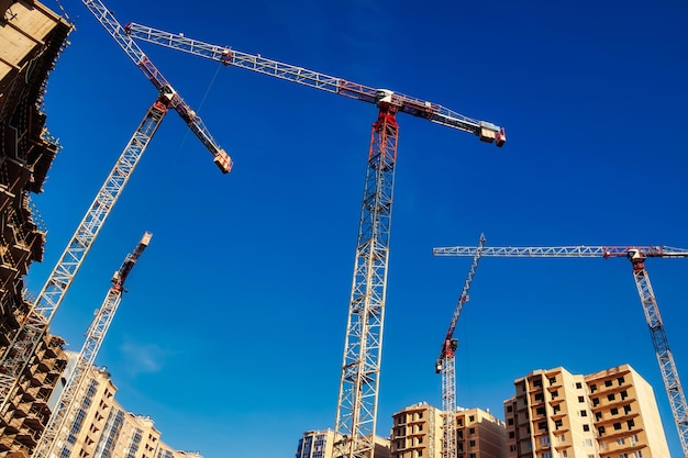 Les grues de construction travaillent sur le site de création sur fond de ciel bleu Vue de dessous de la grue industrielle Concept de construction d'immeubles d'appartements et de rénovation de logements Espace de copie