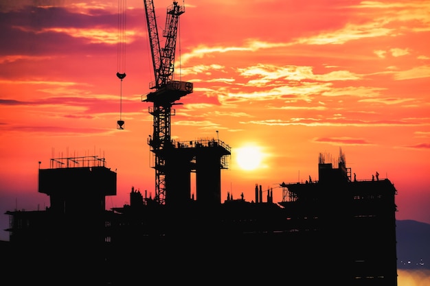 Photo des grues en silhouette sur le chantier au coucher du soleil