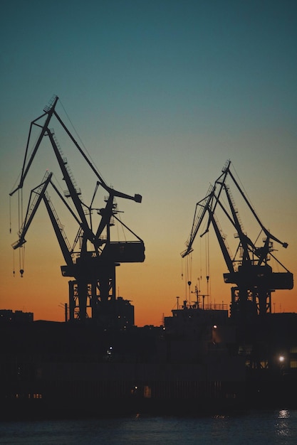 Photo des grues en silhouette sur un quai commercial contre le ciel au coucher du soleil