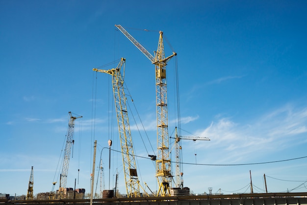 Grues à tour au-dessus des bâtiments en construction contre le ciel bleu. Image de gros plan de construction avec espace de copie. Construction de la ville.