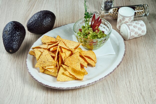 Guacamole épicé à l'avocat avec des chips de nacho sur une plaque lumineuse sur une table en bois. Vue rapprochée sur une collation mexicaine populaire