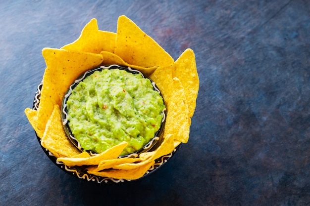 Guacamole sauce mexicaine traditionnelle avec chips tortilla dans un bol en argile. Bol de guacamole avec chips de nachos sur fond sombre. Espace de copie. Vue de dessus