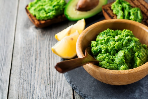 Guacamole sauce mexicaine traditionnelle dans un bol en bambou, citron et demi avocat coupé sur une vieille surface en bois. Mise au point sélective. Lieu de texte.