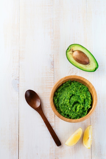 Guacamole sauce mexicaine traditionnelle dans un bol en bambou, citron et moitié avocat coupé sur une surface en bois blanche. Mise au point sélective. Lieu de texte.