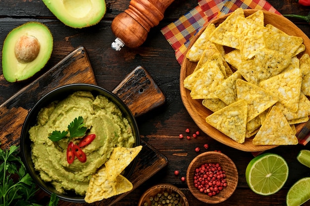 Guacamole. Sauce trempette mexicaine latino-américaine traditionnelle dans un bol noir avec avocat et ingrédients et nachos de maïs