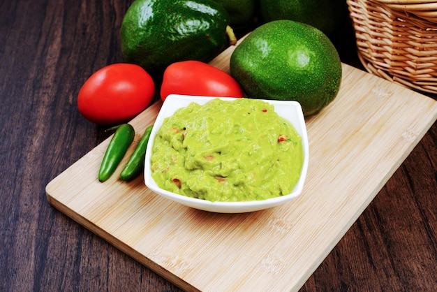 Photo guacamole servi sur une assiette blanche sur une table en bois. ingrédients du guacamole.