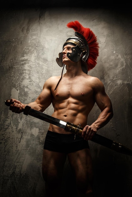 Guerrier musclé avec épée et casque posant devant un mur de béton