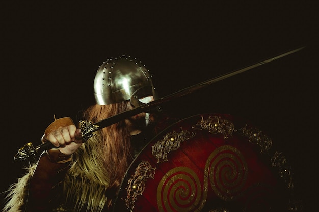 Guerrier nordique et viking avec casque métallique et peaux d'animaux. gantelets en cuir, bouclier en bois rouge avec décorations dorées et épée en acier