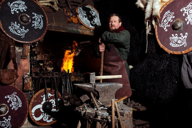 Le guerrier viking est près du feu dans sa forge avec des armes à la main.