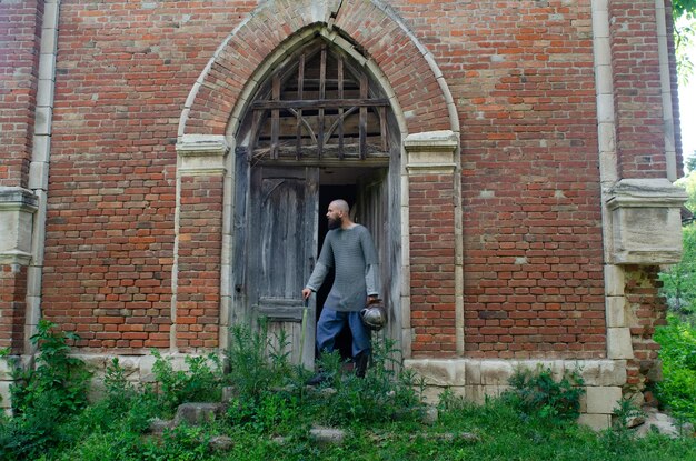 Guerrier viking près d'un vieux château en brique Épée et casque Regard pensif Vieille porte en bois