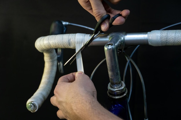 Guidon de vélo de route sur fond noir Installer du ruban de guidon blanc Réparation de vélos dans un atelier moderne Mécanicien dans les mains de l'atelier et gros plan de ruban isolant blanc