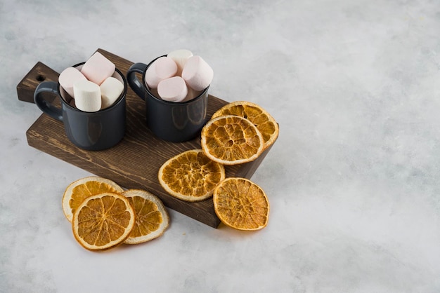 Guimauve avec du café dans une tasse avec des tranches d'orange séchées sur une plaque de bois de coupe