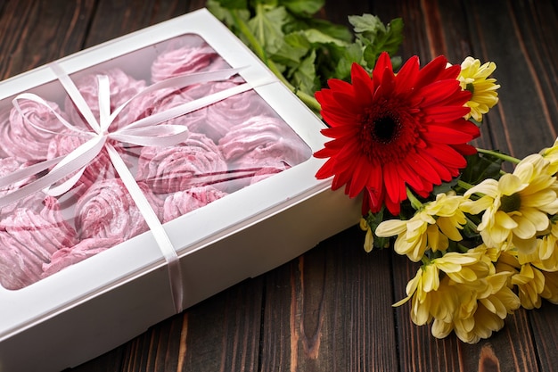 Guimauve rose, emballée dans une boîte avec un ruban et des fleurs, pour un cadeau, sur une planche de bois