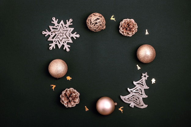 Guirlande de décorations de Noël dorées - boules brillantes, arbre de Noël, pommes de pin et flocon de neige sur fond de papier noir. Vue de dessus, pose à plat, espace de copie