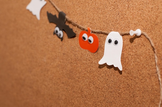 Guirlande d'Halloween faite maison sous forme de fantômes de citrouilles et de chauves-souris avec des yeux sur un fond de planche de liège
