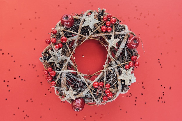 Guirlande de Noël faite de branches décorées d'étoiles en bois d'or et de bulles de fruits rouges isolés sur fond rouge