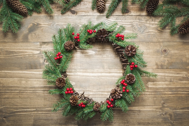 Guirlande de Noël faite de branches d'épinette avec baies de houx sur planche de bois.