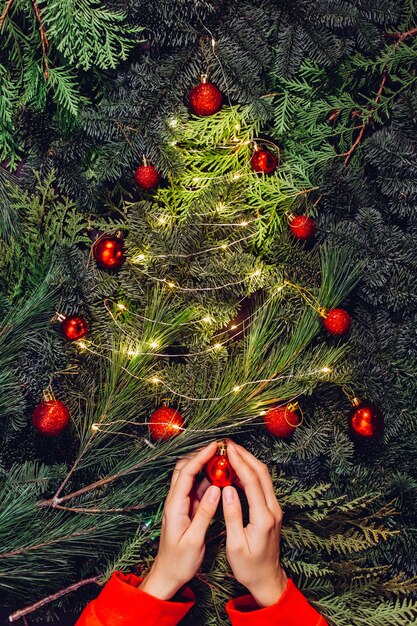 Guirlande de Noël, gros plan des mains féminines fait une couronne d'épinette et décore avec des boules rouges,