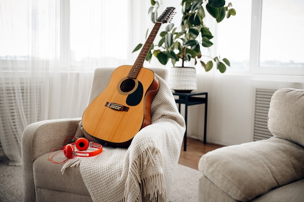 Guitare et casque sur fauteuil blanc à la maison, personne. Instrument de musique acoustique et écouteurs dans la chambre, concept de mélomanes