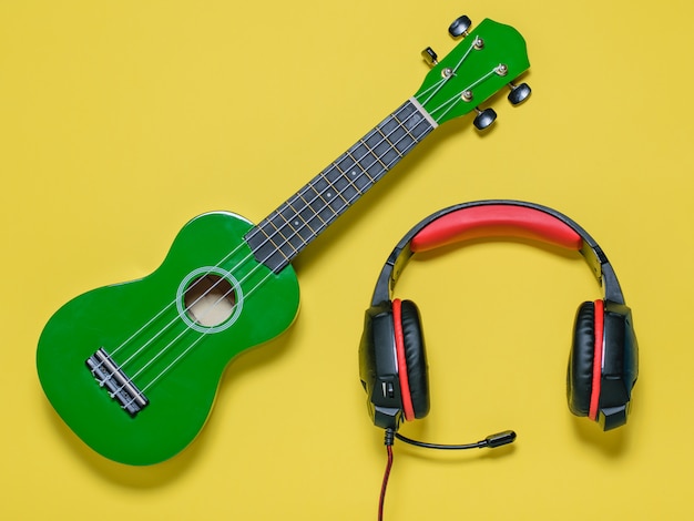 Guitare ukulélé vert et casque rouge-noir sur fond jaune. La vue du haut.