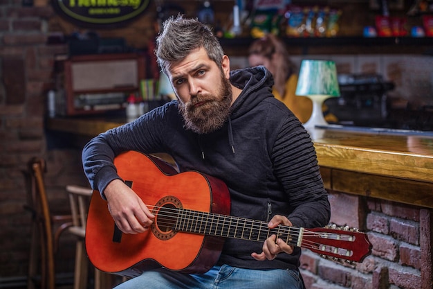 Guitares et cordes Homme barbu jouant de la guitare tenant une guitare acoustique dans ses mains Concept musical Le guitariste barbu joue Jouer de la guitare Barbe hipster homme assis dans un pub Musique live