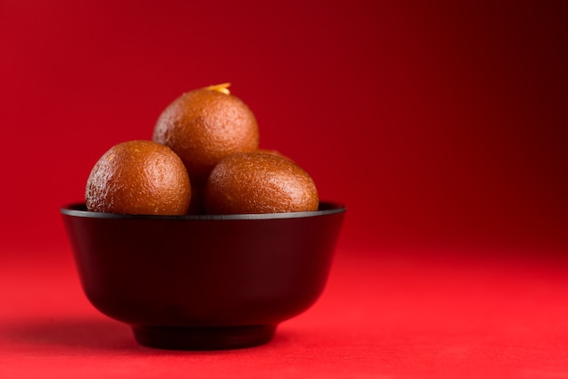 Gulab Jamun dans un bol noir sur fond rouge. Dessert indien ou plat sucré.