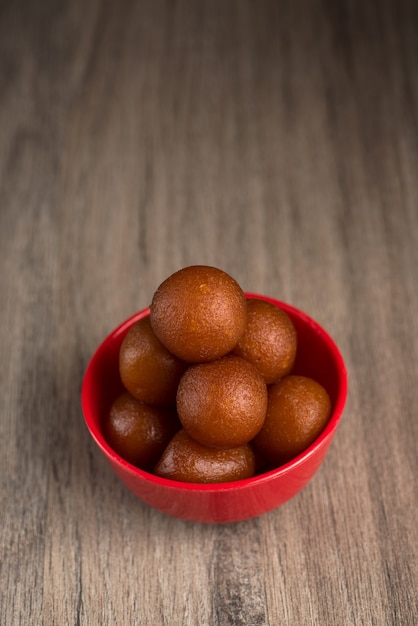 Gulab Jamun dans un bol rouge sur bois. Dessert indien ou plat sucré.