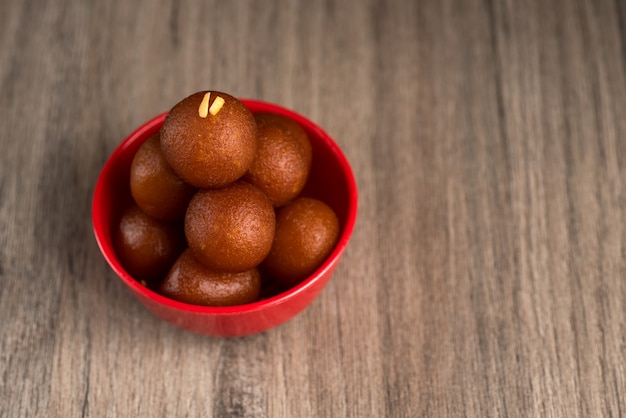 Gulab Jamun dans un bol rouge sur bois. Dessert indien ou plat sucré.