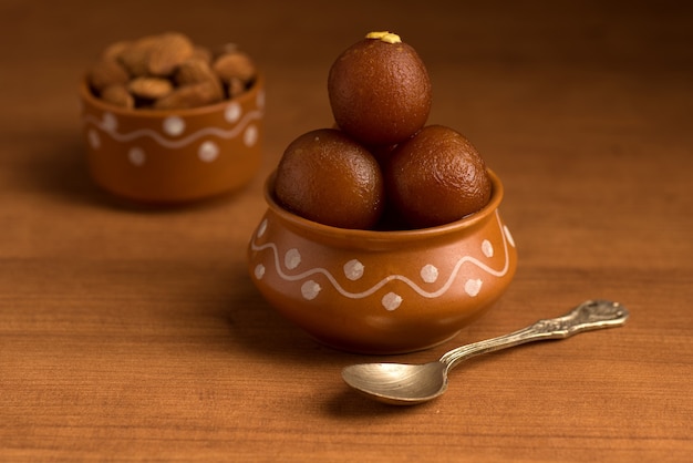 Gulab Jamun en pot d'argile avec cuillère et fruits secs. Dessert indien ou plat sucré