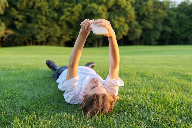 Guy adolescent allongé sur l'herbe avec smartphone Homme en T-shirt blanc avec téléphone dans ses mains vue de dessus fond de pelouse verte