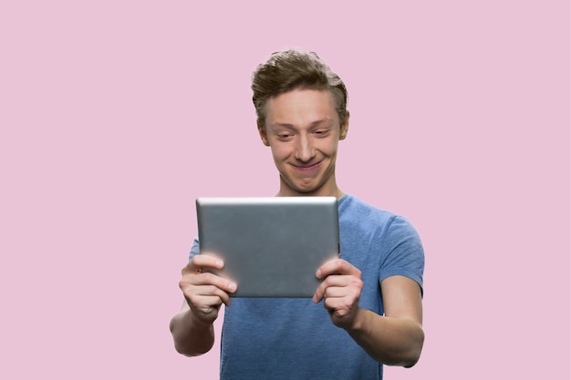 Guy américain souriant en regardant la tablette. Écolier caucasien isolé sur fond rose.