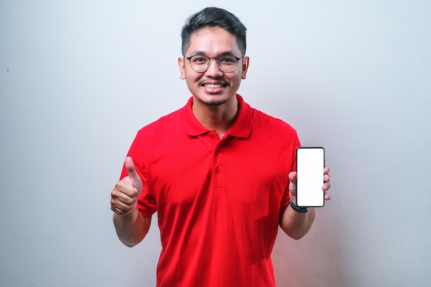 Guy asiatique portant une chemise rouge sourire à la caméra montrant l'écran vide du smartphone recommandant l'application