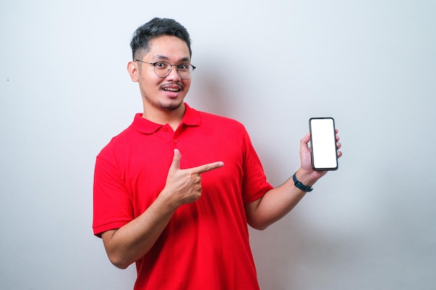 Guy asiatique portant une chemise rouge sourire à la caméra montrant l'écran vide du smartphone recommandant l'application