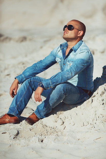 Guy assis sur le sable, un jean tanné