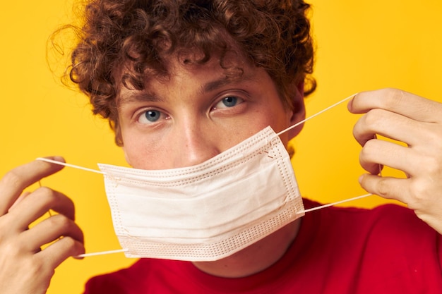 Guy aux cheveux bouclés rouges dans des masques de protection sécurité posant fond jaune inchangé