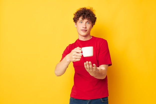 Guy aux cheveux bouclés rouges tasse blanche dans les mains d'un verre fond jaune inchangé