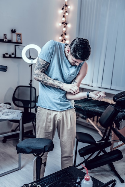 Guy ayant des inconvénients. Homme aux cheveux noirs observant son tatouage fraîchement fait sur son poignet tout en restant dans l'armoire principale