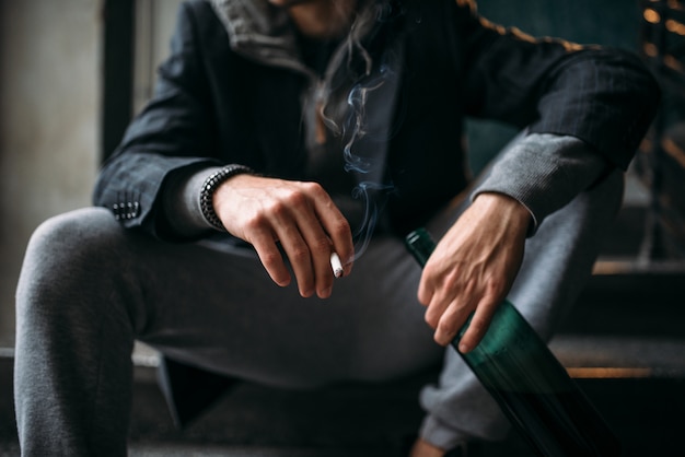 Guy avec bouteille est assis sur les escaliers et fumer