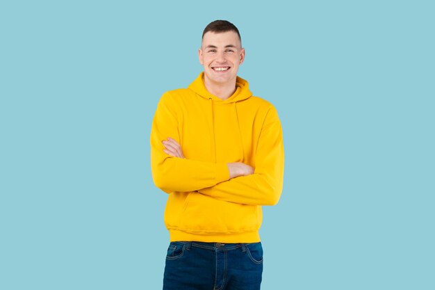 Guy caucasien excité posant avec les bras croisés et souriant à la caméra sur l'espace libre de fond de studio bleu